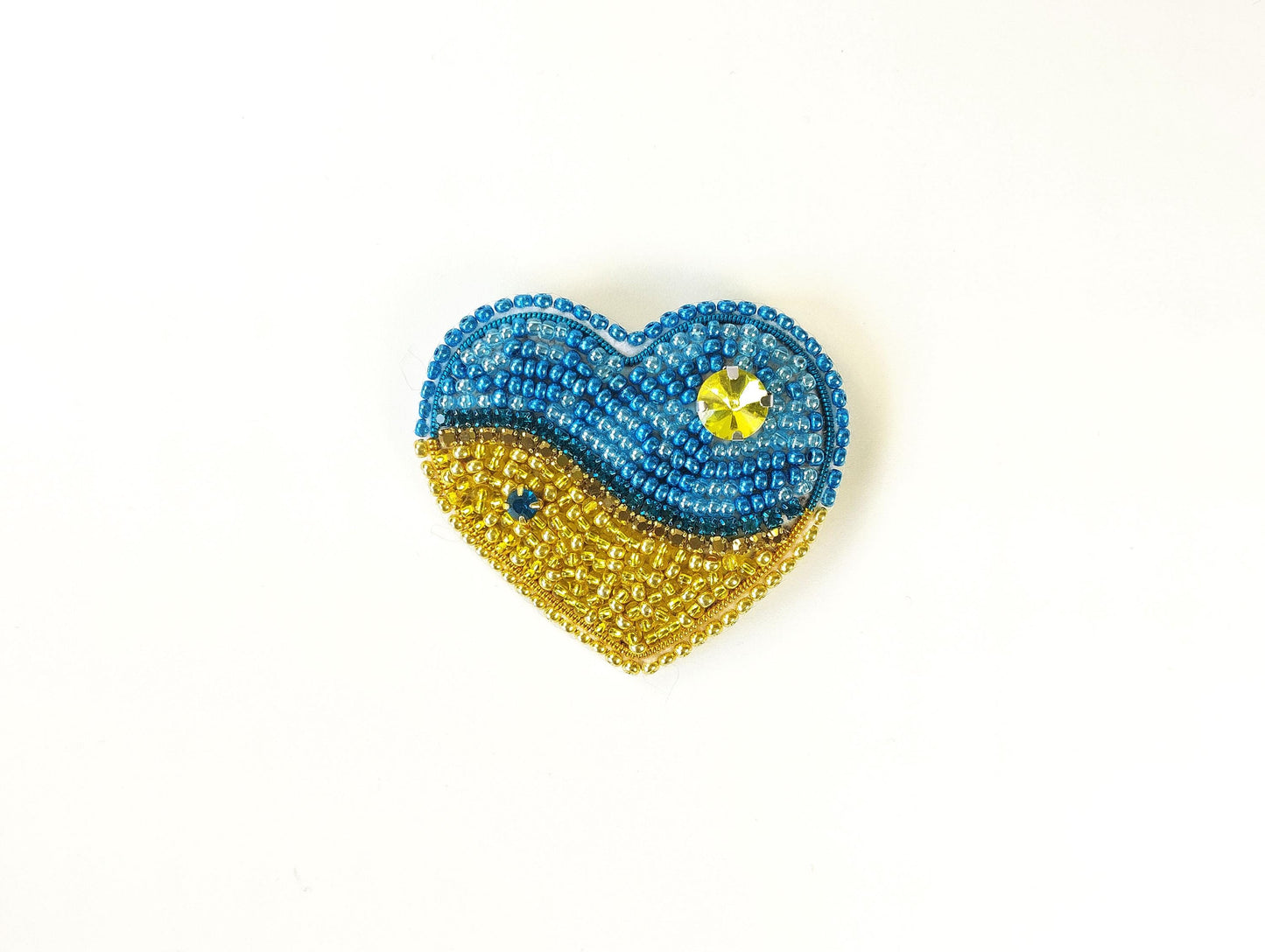 a beaded heart shaped brooch with a blue and yellow design