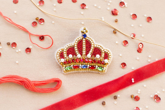 a red ribbon, a crown-shaped embellishment, and various beads and sequins on a beige background.