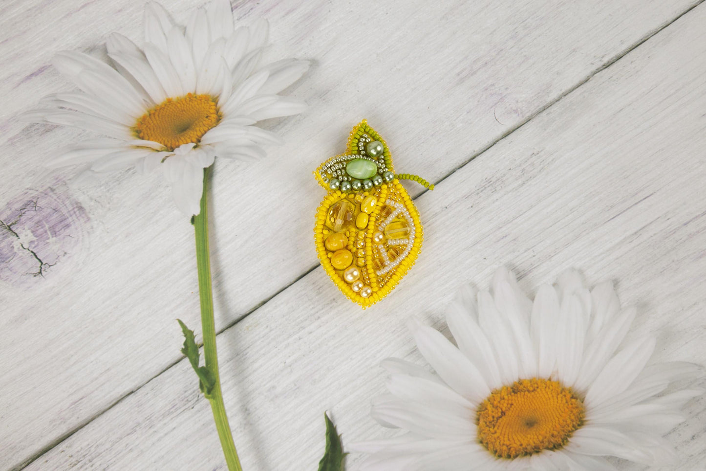 two daisies and a brooch sitting on a white wooden surface