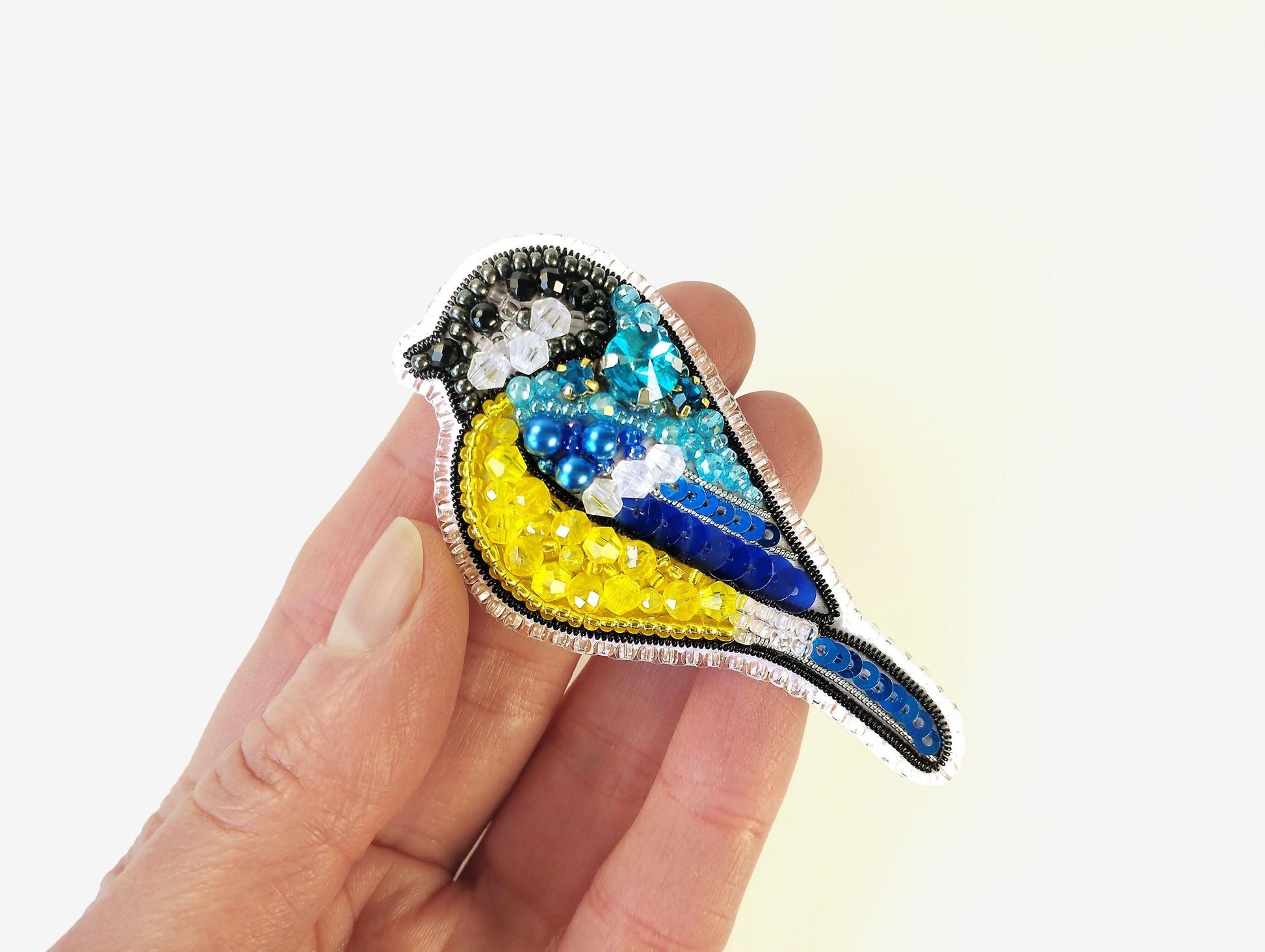 a hand holding a brooch with a bird on it