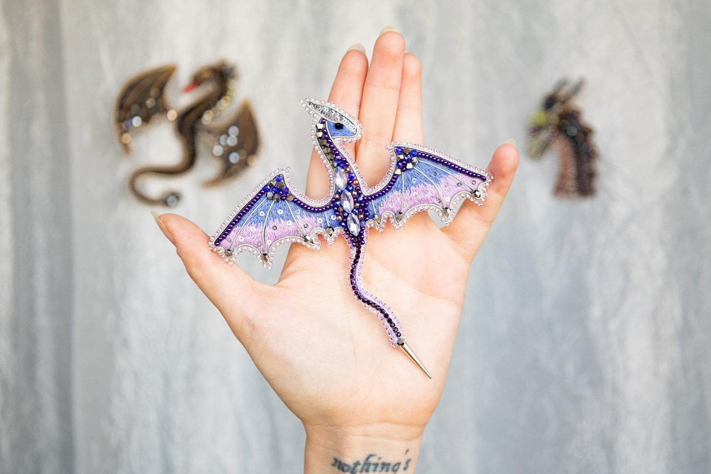 a hand holding a purple and blue dragon brooch
