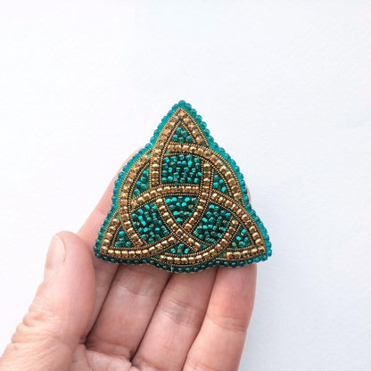 A hand holding a triangular beaded object with a geometric pattern.
