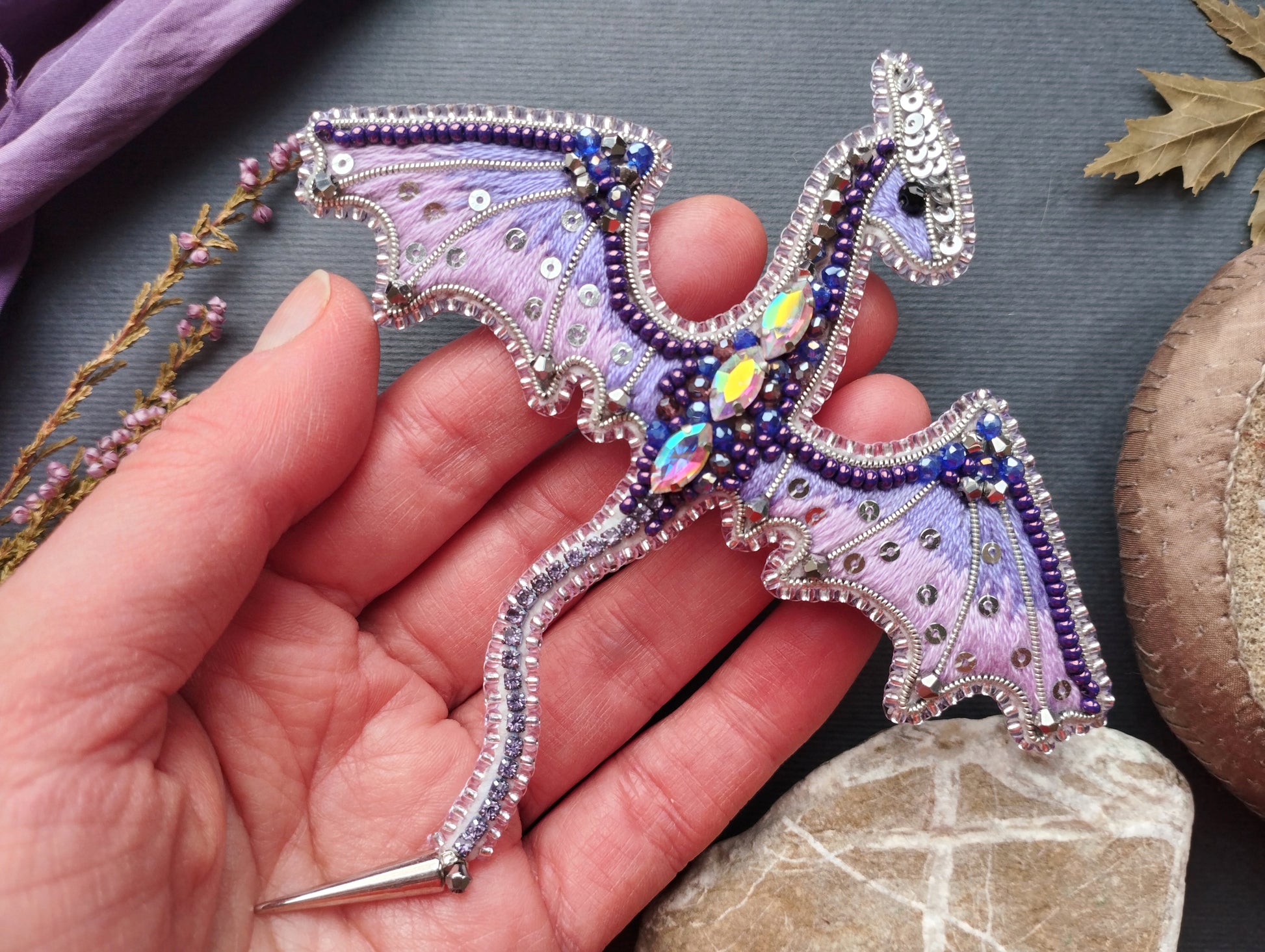 A hand holding a decorative dragon-shaped piece of jewelry, which appears to be made of beads and other embellishments.