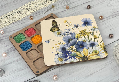 a box of beads next to a paint palette with a butterfly on it