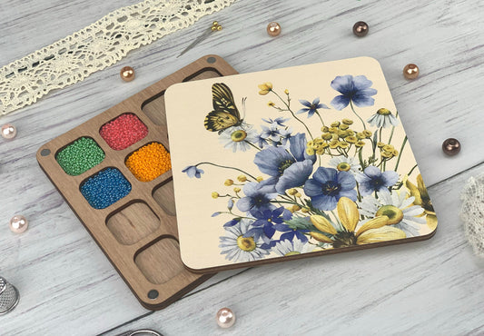 a box of beads next to a paint palette with a butterfly on it