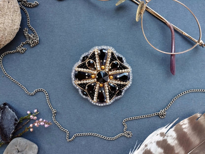 a collection of jewelry and accessories, including a brooch with a black and gold design, a pair of glasses, a necklace, and a feather, all arranged on a blue background.