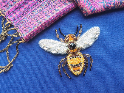 A close-up view of a beaded and embroidered bee pin on a blue fabric background.