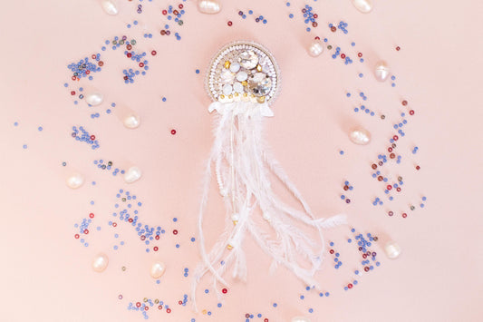 a decorative piece with a white and gold design, surrounded by various colorful beads and pearls on a light pink background.