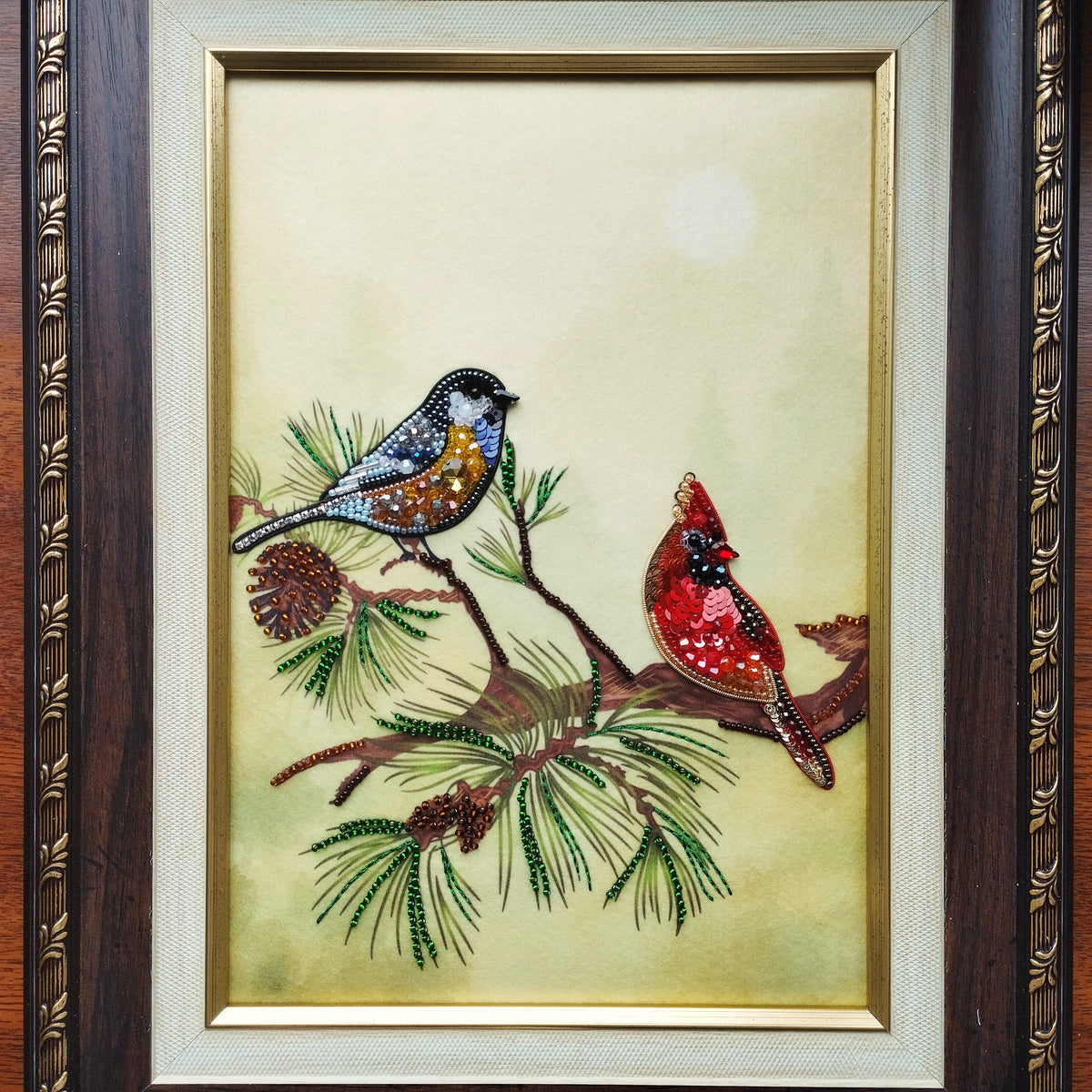 The image is a framed painting depicting two birds perched on a branch with pine needles and pine cones.