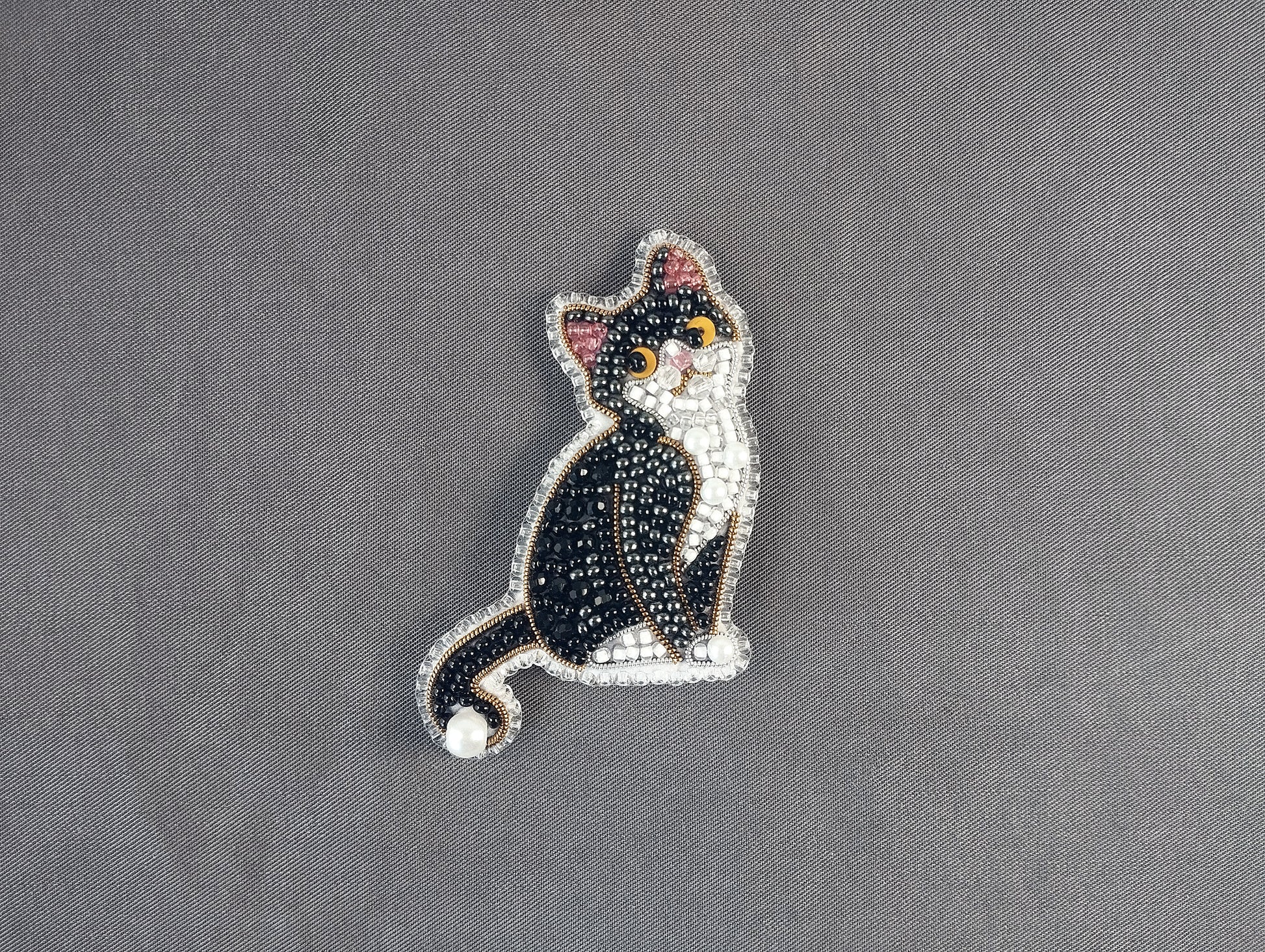 A decorative cat brooch made of beads and glitter, featuring a black and white color scheme.