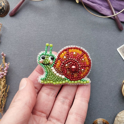 A hand holding a colorful beaded snail-shaped object against a gray background.
