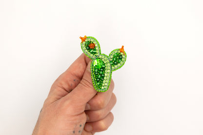 a hand holding a green brooch with a cactus on it