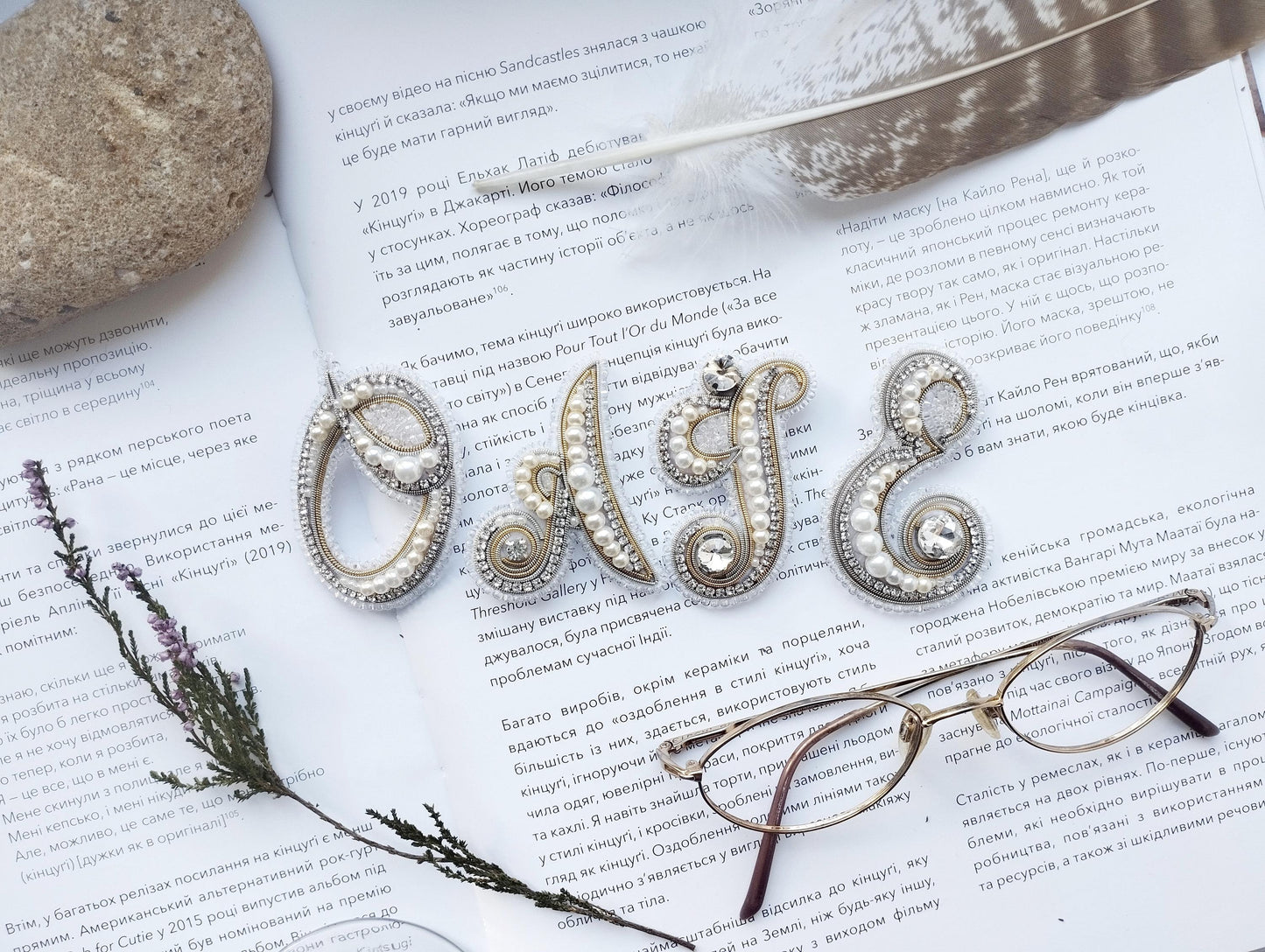 a close-up of a book with text in Russian, a feather, a pair of glasses, and some decorative elements such as pearls and beads.