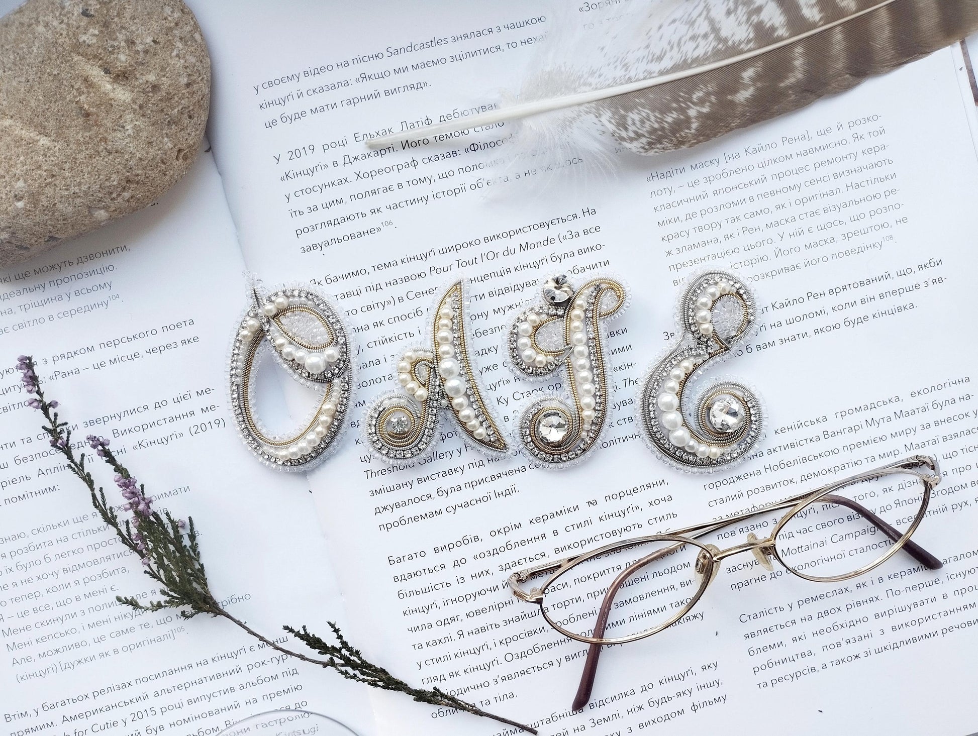 a close-up of a book with text in Russian, a feather, a pair of glasses, and some decorative elements such as pearls and beads.
