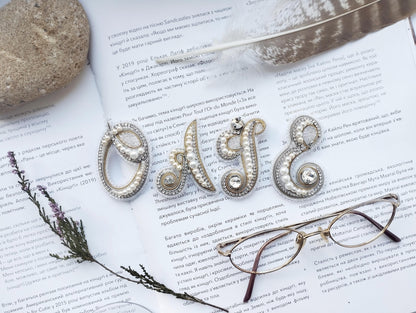 a close-up of a book with text in Russian, a feather, a pair of glasses, and some decorative elements such as pearls and beads.