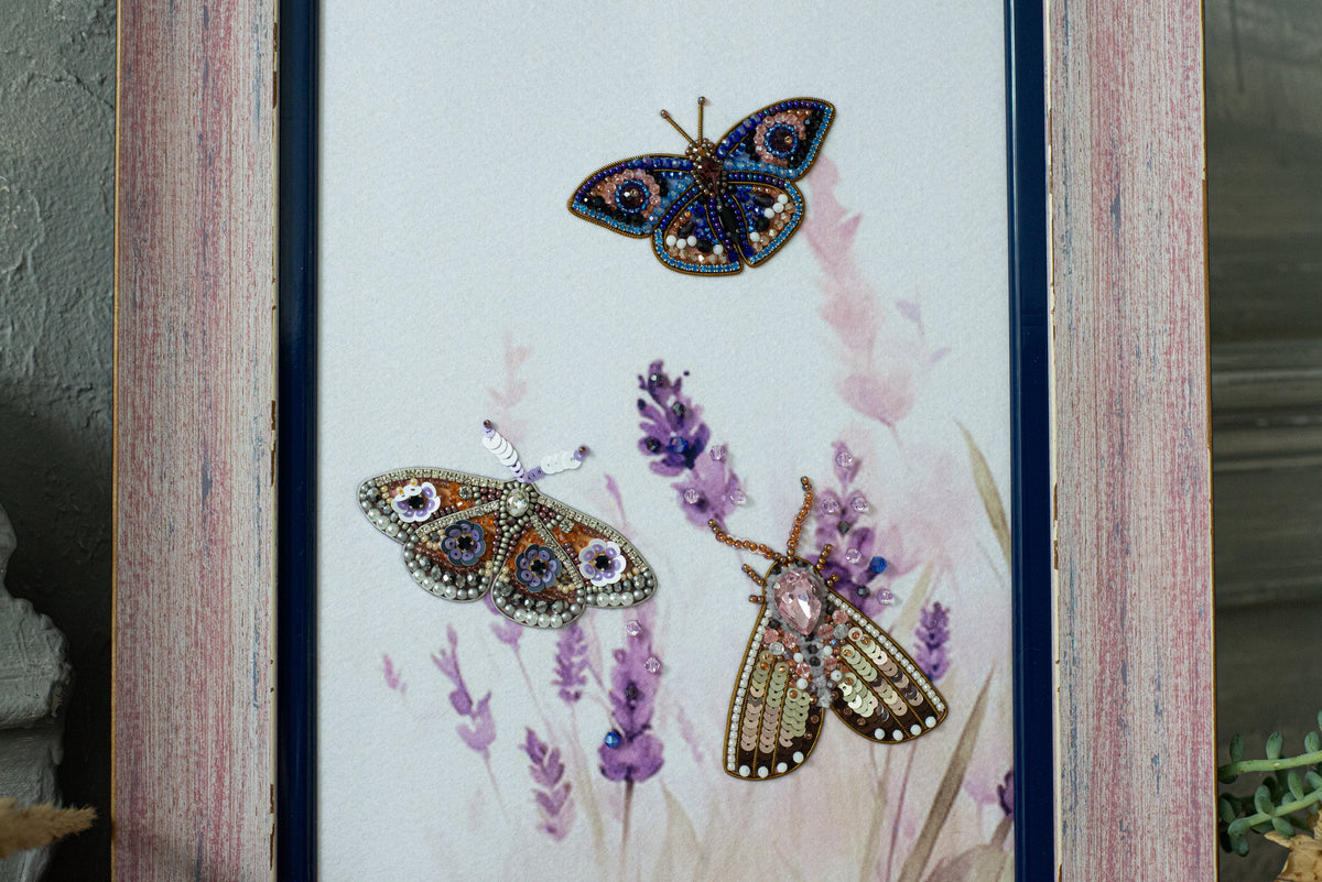 three butterflies with intricate beading and embroidery designs, set against a background of purple flowers.