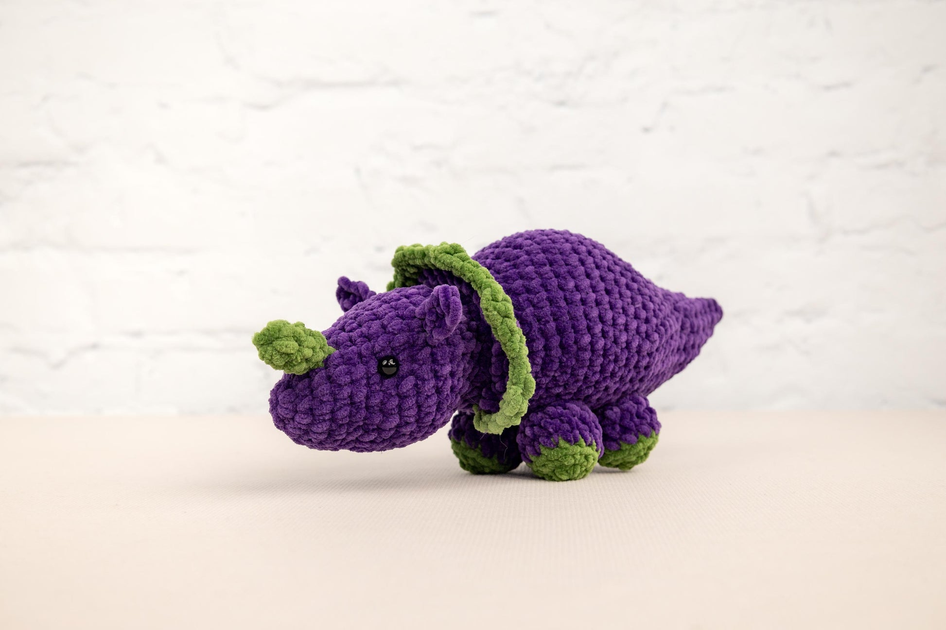 a purple crocheted rhinoceros with a green tail