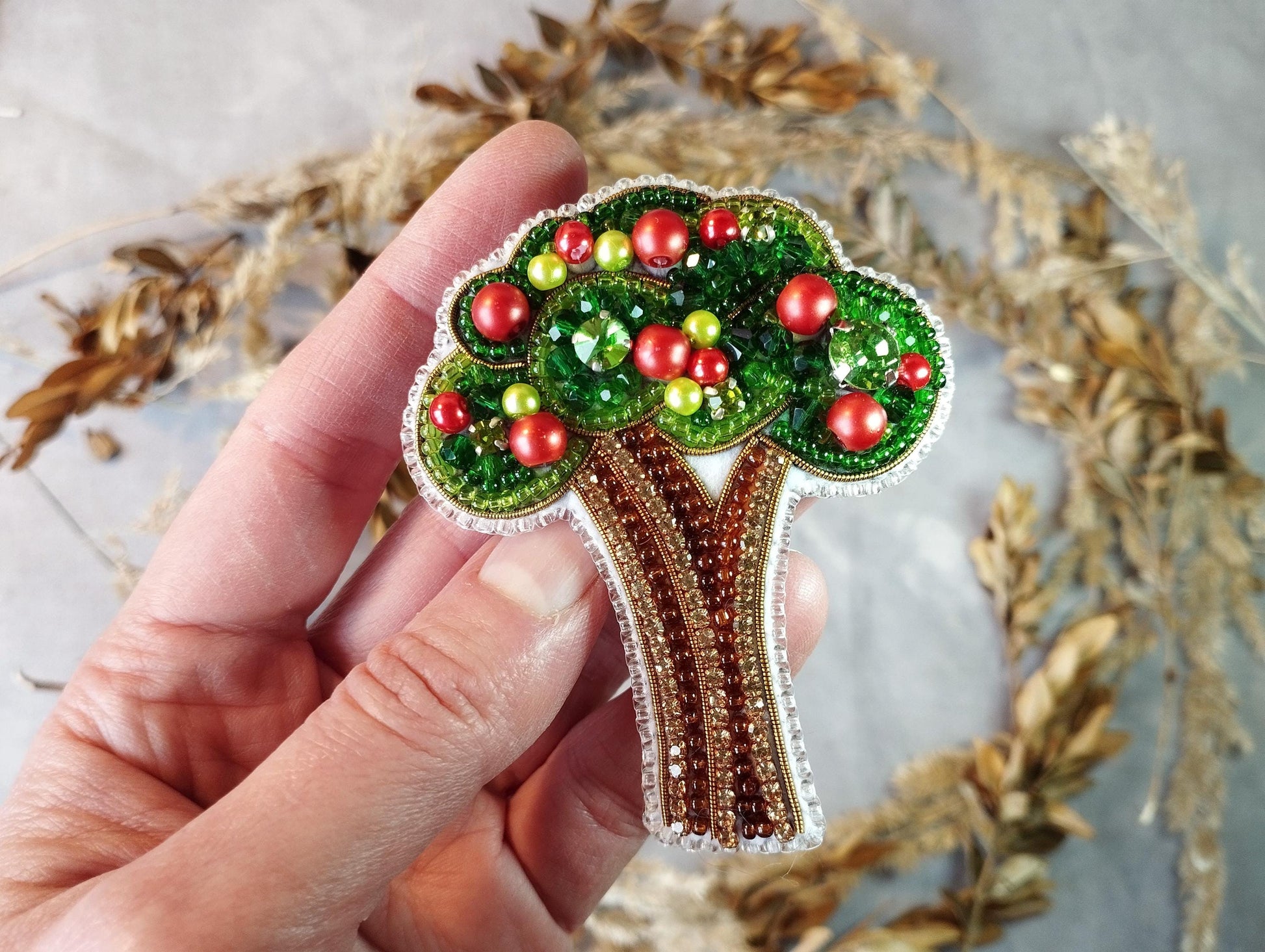 a hand holding a brooch with a tree on it