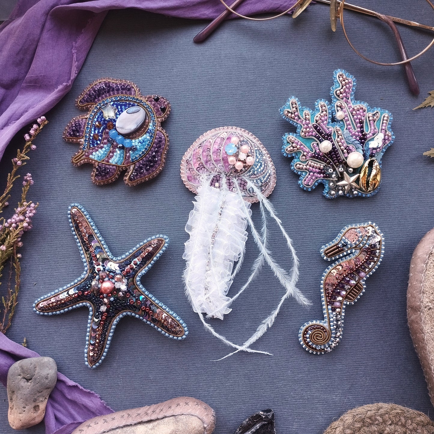 a collection of five intricately designed sea-themed brooches or pins, each with unique patterns and embellishments, arranged on a gray background.