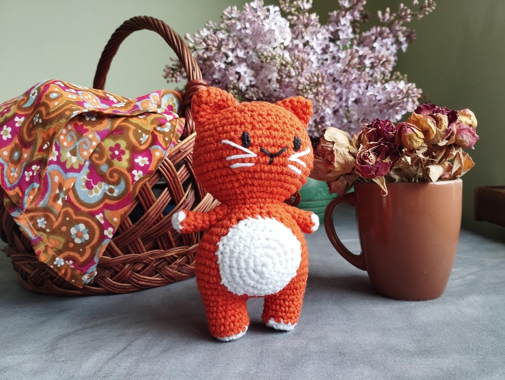 a crocheted cat next to a basket of flowers