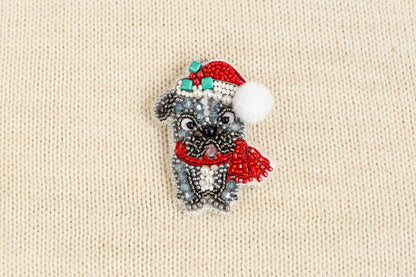 A small, intricately beaded dog wearing a red Santa hat and scarf is displayed on a beige textured background.