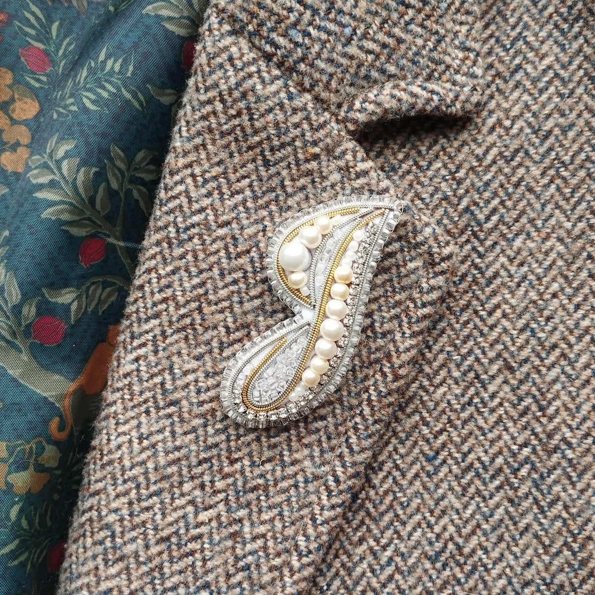 a close-up view of a tweed jacket with a decorative brooch or pin attached to the lapel.