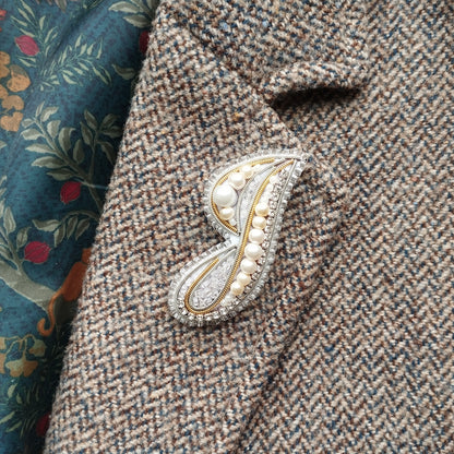 a close-up view of a tweed jacket with a decorative brooch or pin attached to the lapel.