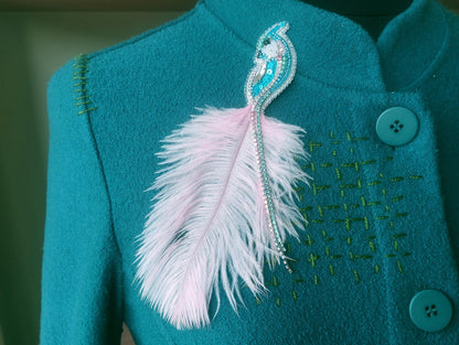 A close-up of a teal-colored jacket with a feather pin and buttons on the front.