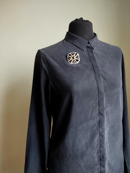 A mannequin wearing a black dress shirt with a decorative brooch on the left side of the chest.