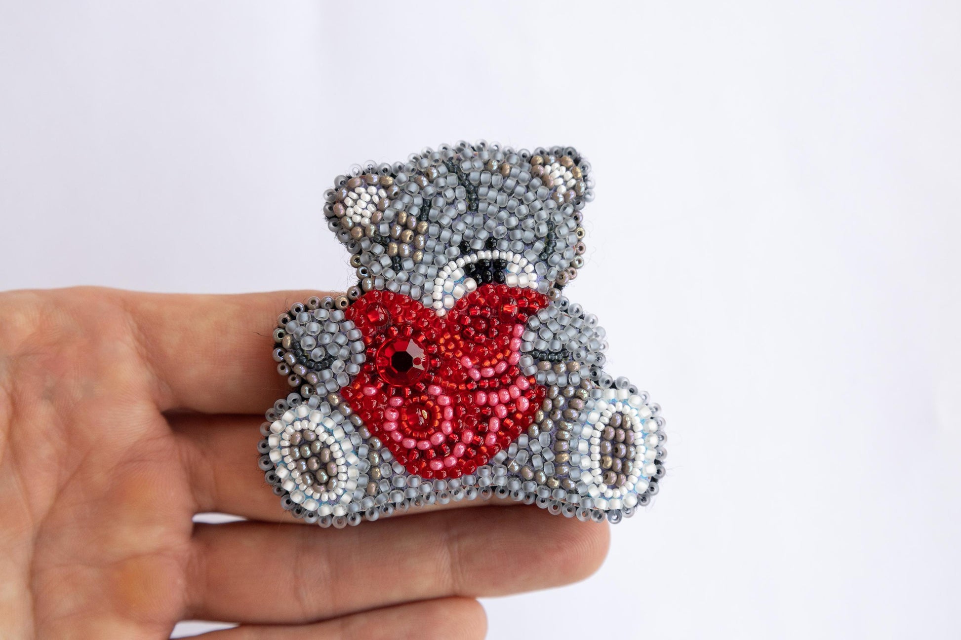 a hand holding a beaded teddy bear with a heart