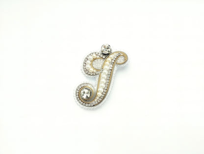 A decorative letter 'J' made of gold, pearls, and crystals against a white background.