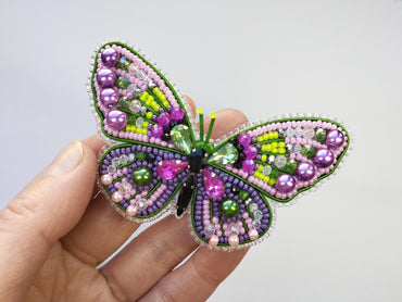 a hand holding a colorful beaded butterfly