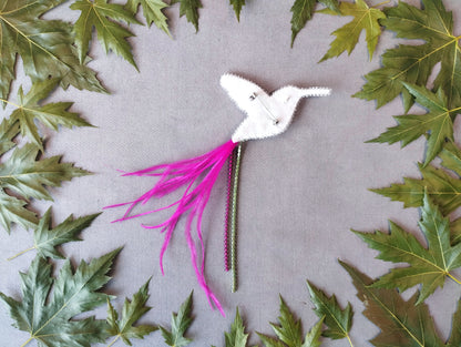 A white bird-shaped object with pink feathers and a green stem is surrounded by green leaves on a gray background.