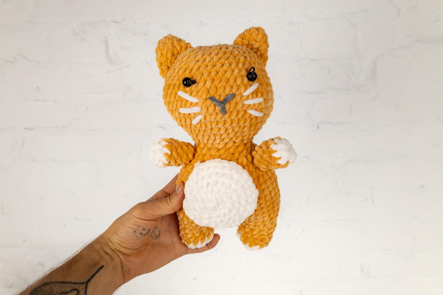 a hand holding a small crocheted cat