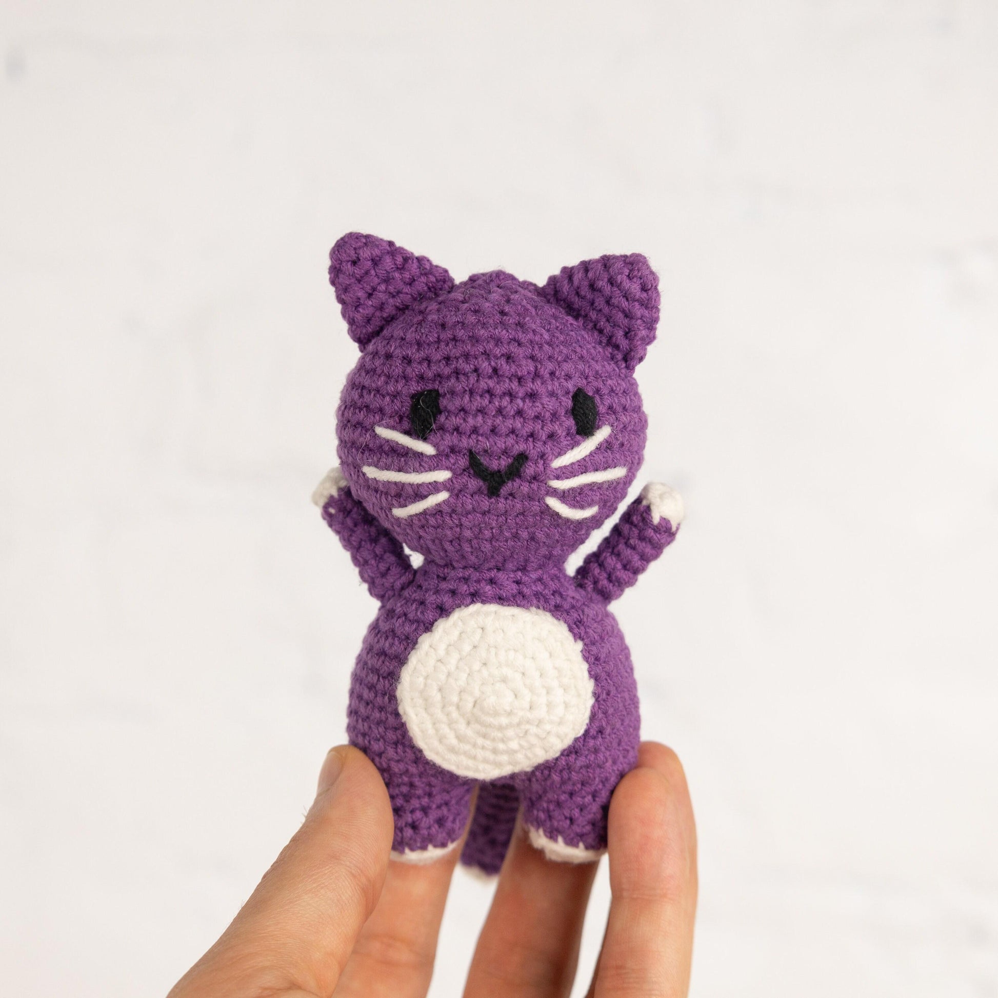 a hand holding a small crocheted purple cat