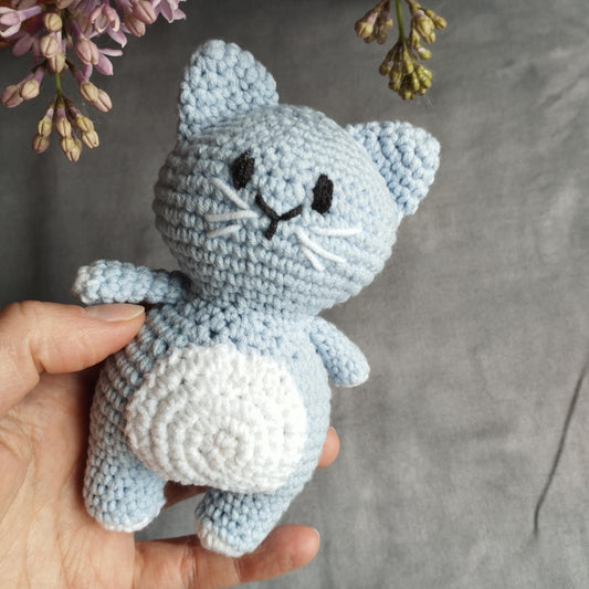 a hand holding a small blue crocheted cat