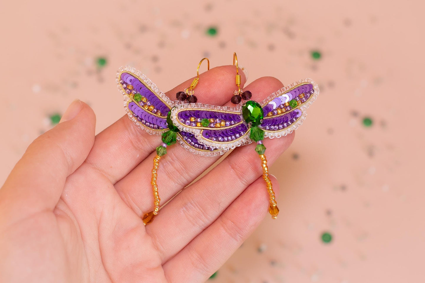 a hand holding a purple and green dragon brooch