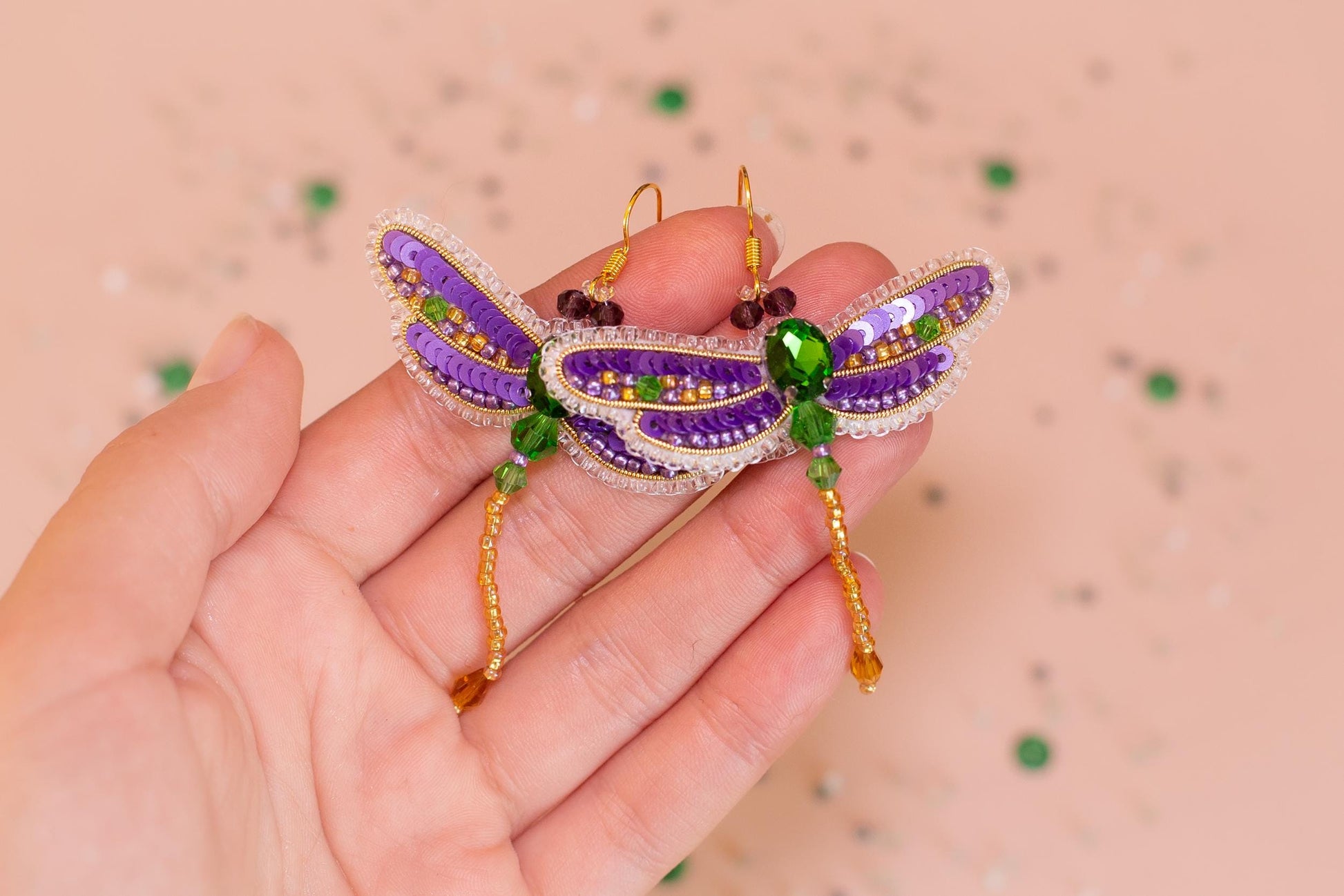 a hand holding a purple and green dragon brooch