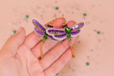 a hand holding a purple and green dragon brooch