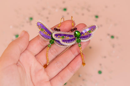 a hand holding a purple and green dragon brooch