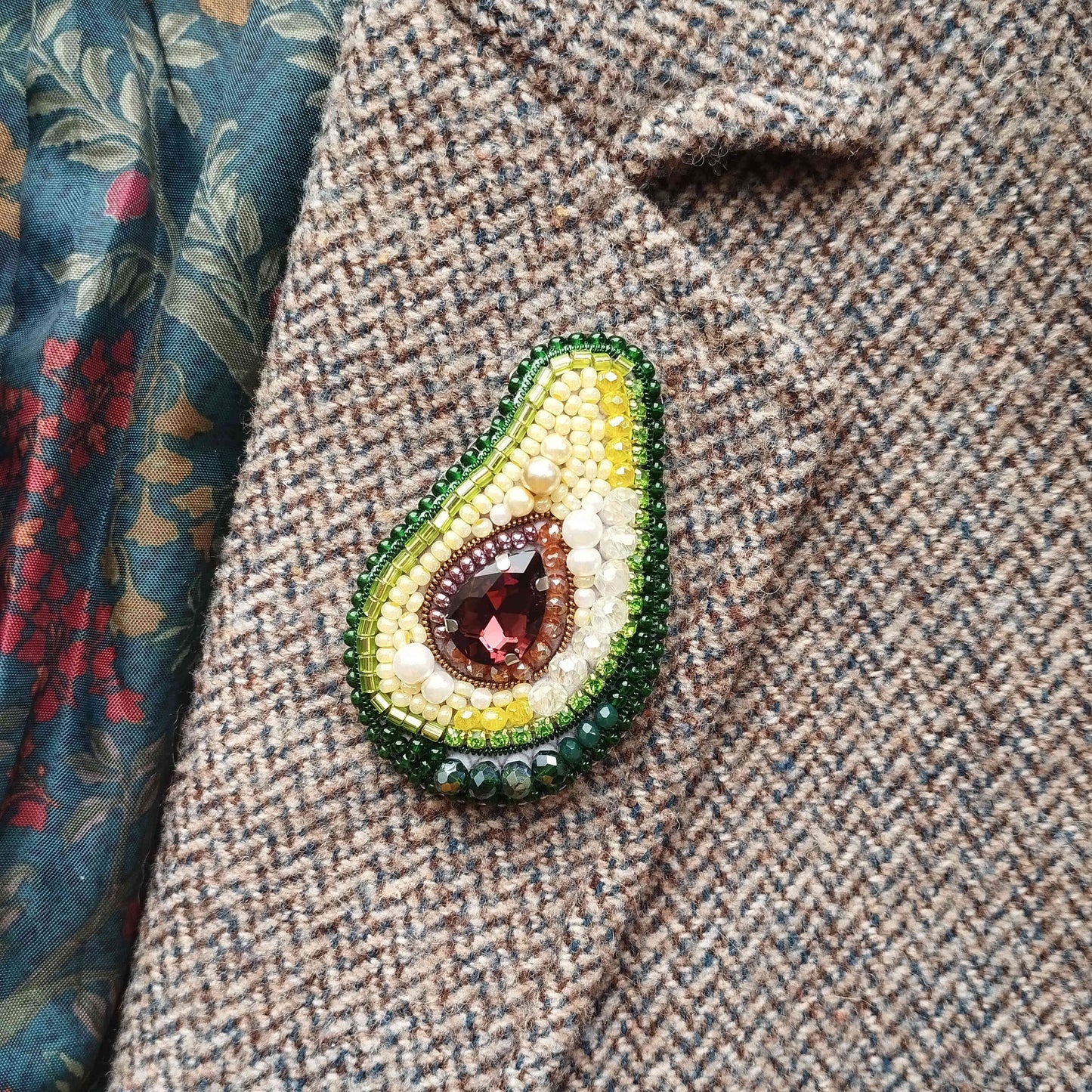 A close-up image of a beaded avocado-shaped brooch on a tweed jacket.