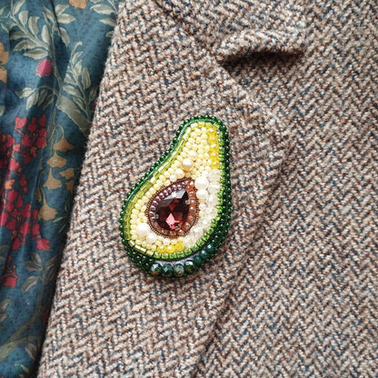 A close-up image of a beaded avocado-shaped brooch on a tweed jacket.