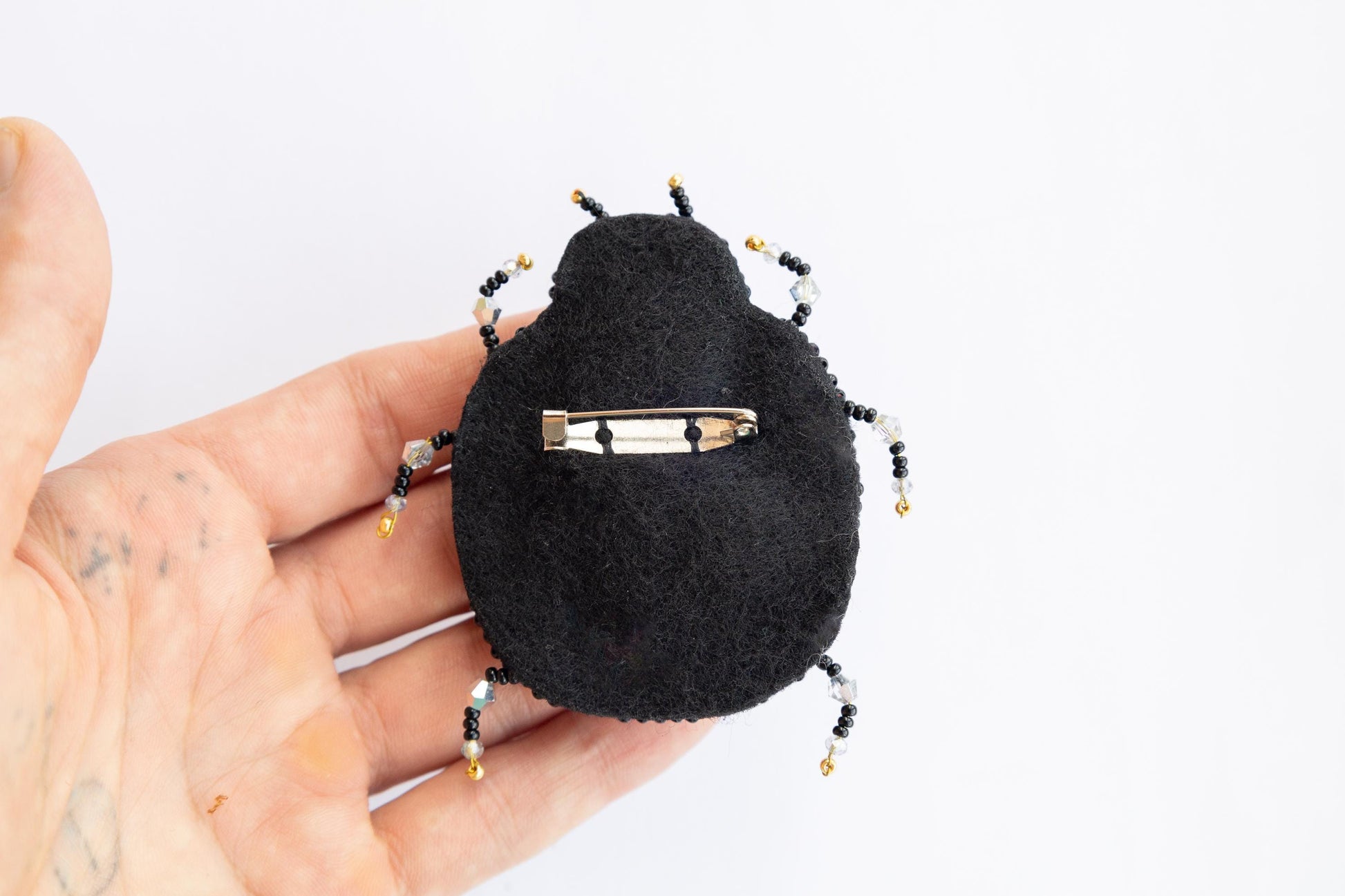 a hand holding a small black beetle brooch