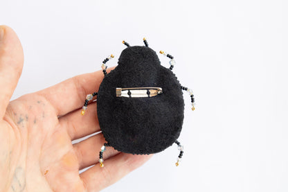 a hand holding a small black beetle brooch