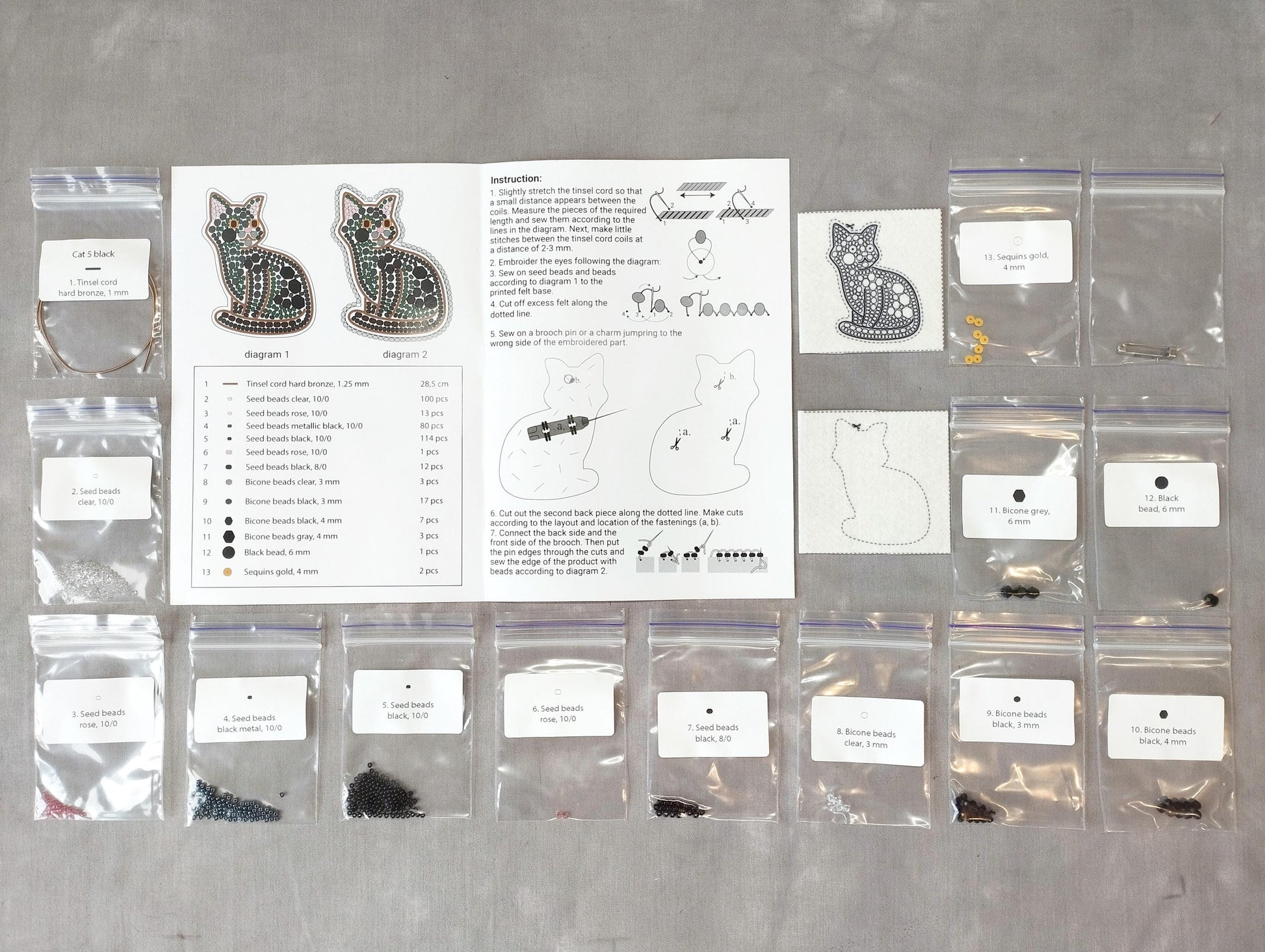 various craft supplies, including bags of beads, seeds, and other materials, arranged on a table. There is also a printed guide or instructions sheet for a project involving cat-themed items, such as earrings and cat-shaped objects.