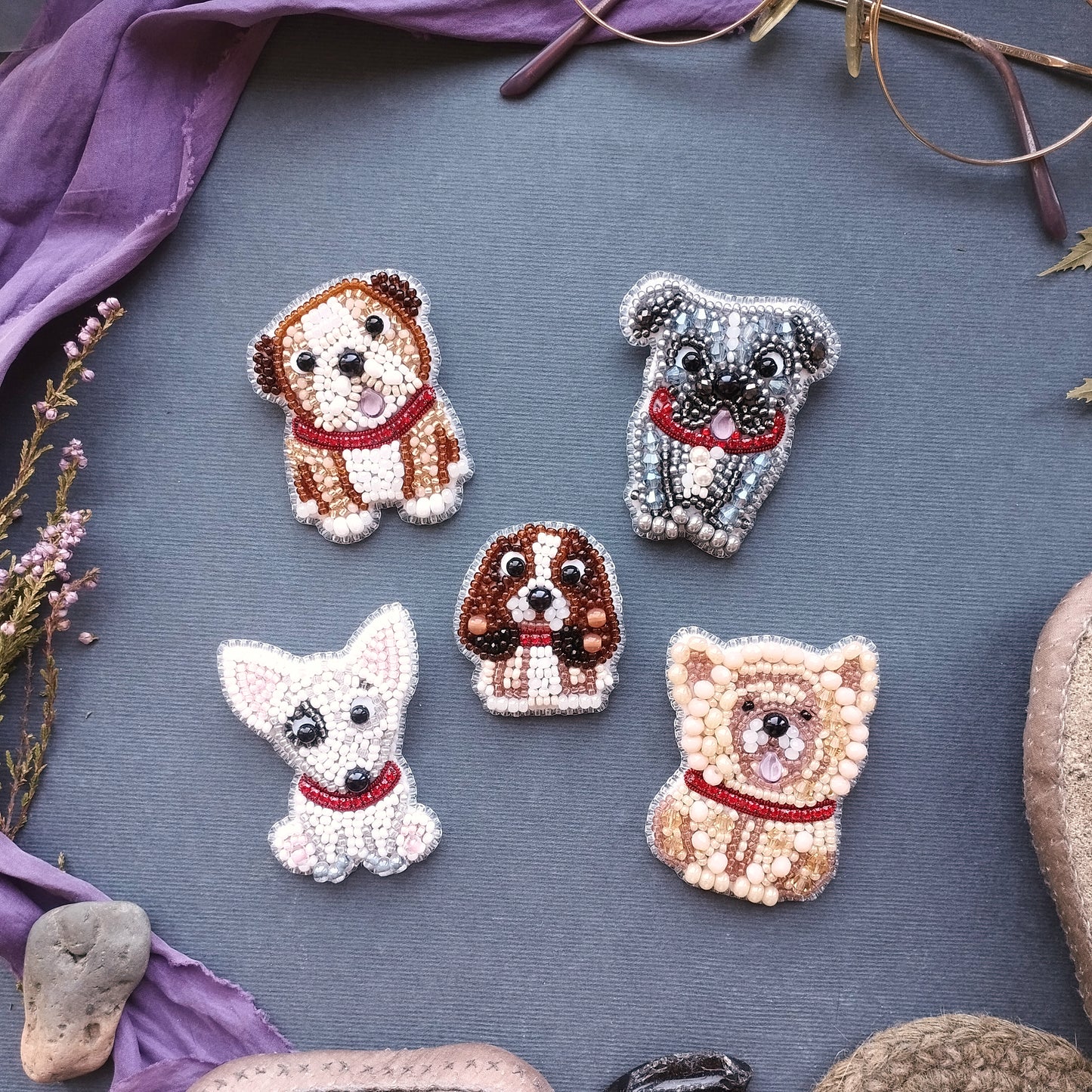 five embroidered dog brooches arranged on a gray background.