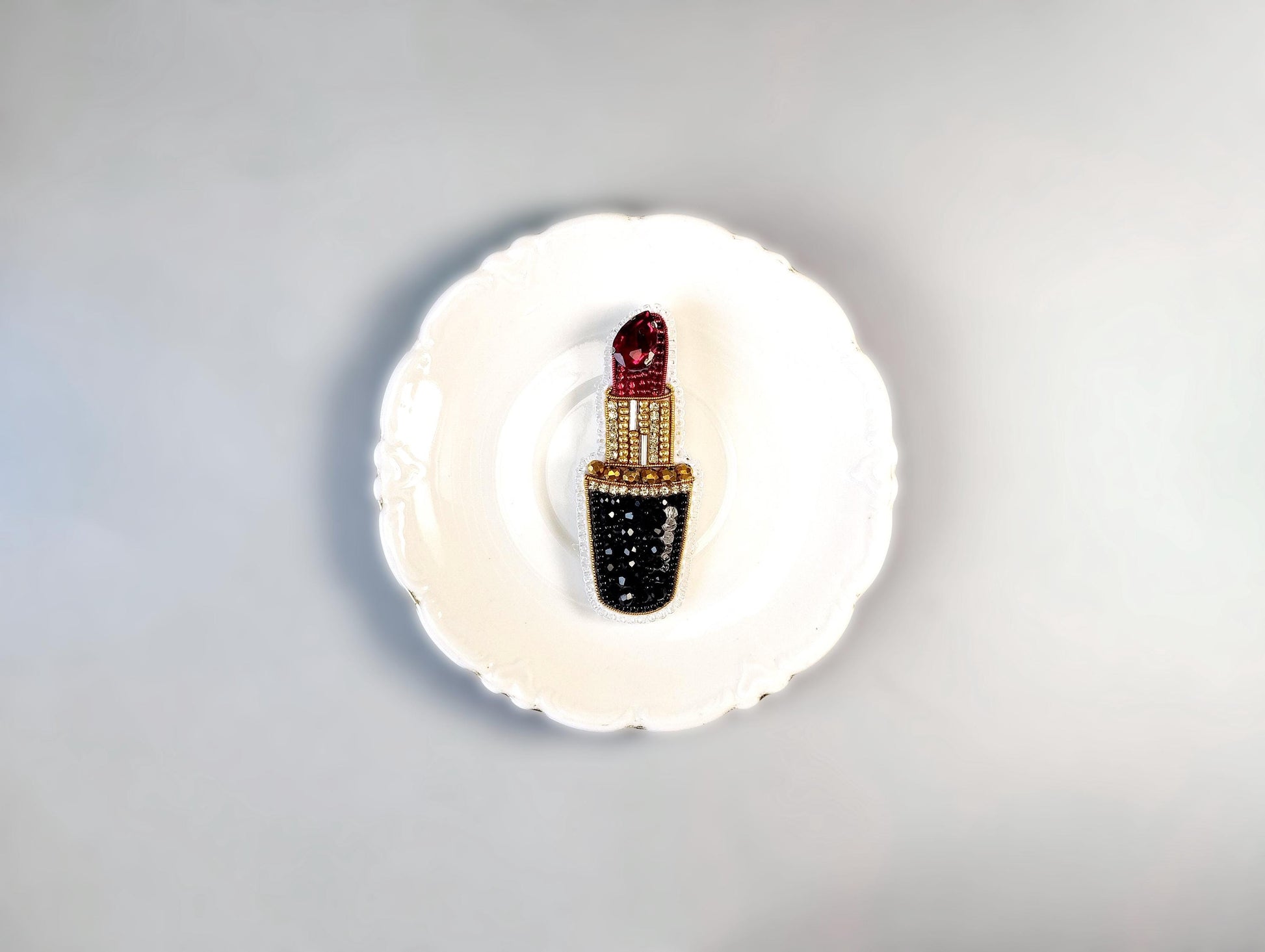 A white plate with a decorative red and black lipstick brooch on it.