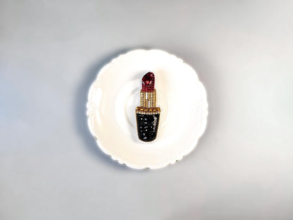 A white plate with a decorative red and black lipstick brooch on it.