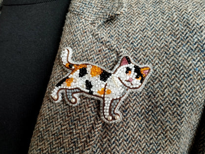 A close-up of a beaded embroidered cat pin on a tweed jacket.