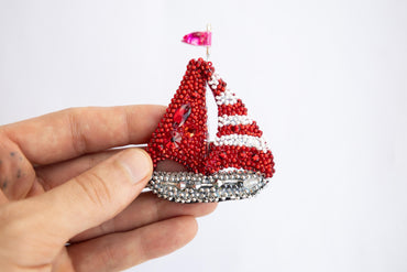 a hand holding a red and white beaded sailboat ornament